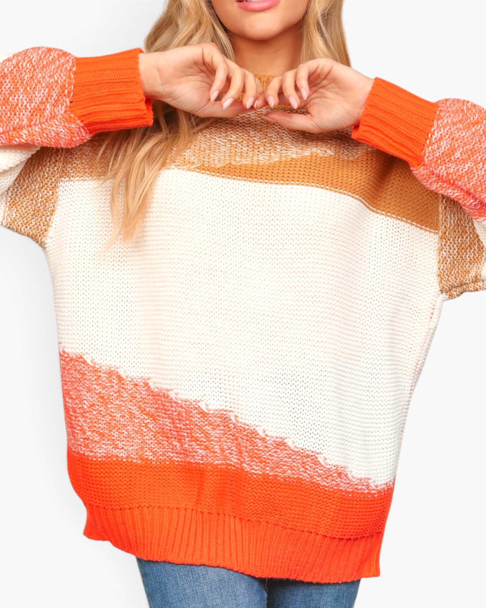 A woman wearing a chunky knit sweater with diagonal stripes in cream, orange, and tan, featuring bright orange ribbed cuffs and hem.