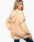 A woman wearing a chunky knit hooded sweater in a light peach-beige color with black embroidered trim details, shown from a three-quarter back view against a plain white background.
