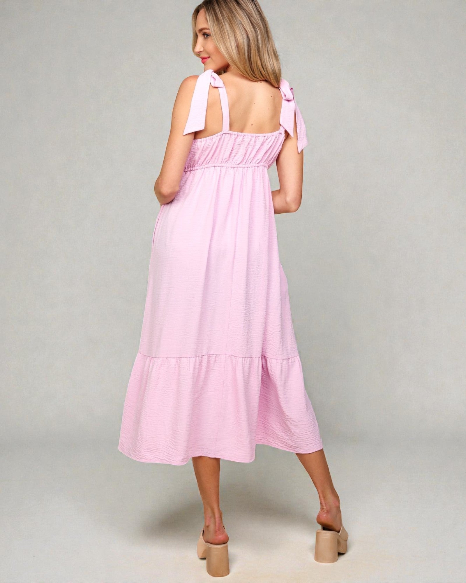 Woman wearing a pink dress with bow straps on a gray background