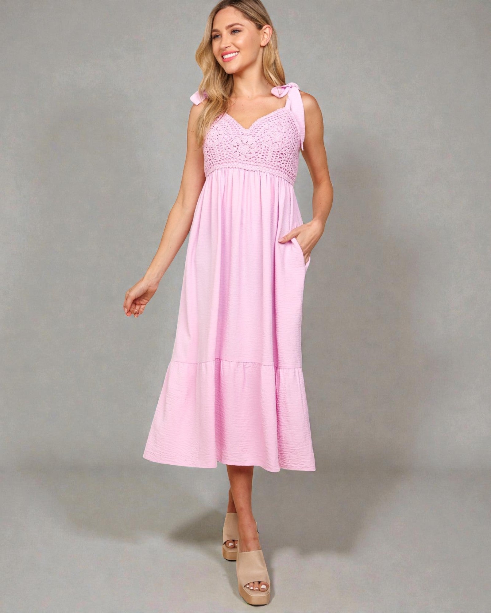 Woman wearing a pink dress with lace details on a gray background