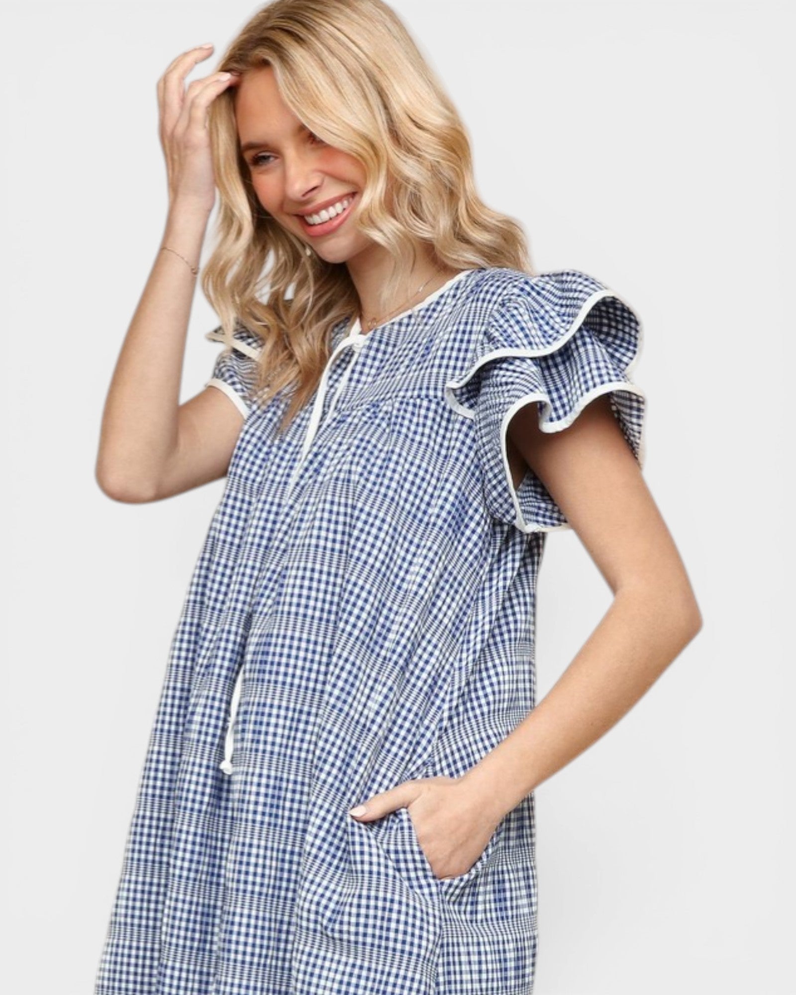 Woman wearing a blue checkered dress with ruffled sleeves on a light gray background