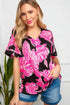 Woman wearing a black and pink floral top with denim shorts against a white wall.