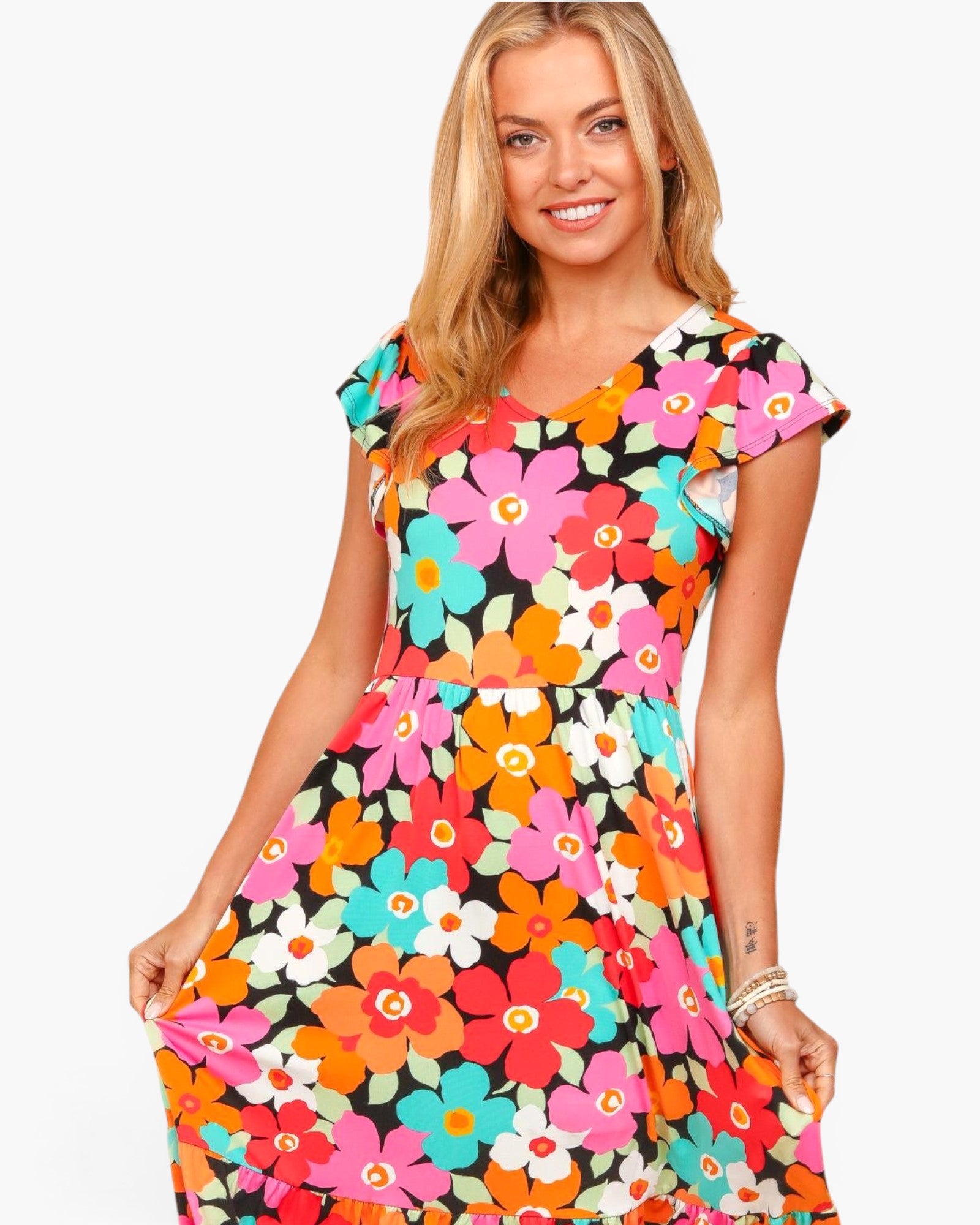 A woman modeling a short-sleeve V-neck dress with a colorful, dense retro floral pattern on a black background, set against a plain white studio backdrop.