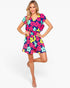 A woman modeling a short-sleeve V-neck romper with a colorful floral print on a light gray studio background.