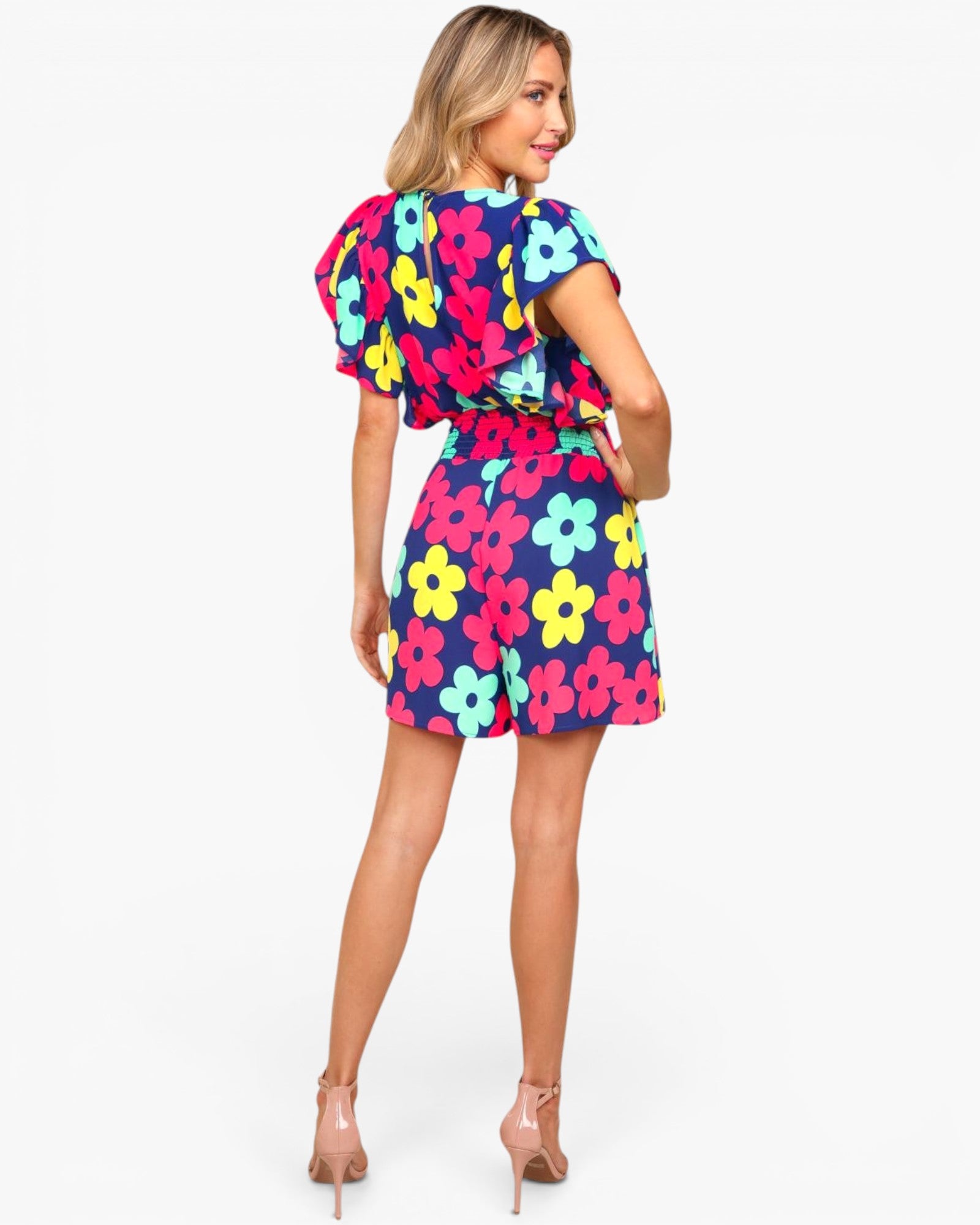 A woman modeling a short-sleeve romper with a colorful floral print, shown from the back against a light gray studio background.