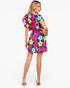 A woman modeling a short-sleeve romper with a colorful floral print, shown from the back against a light gray studio background.