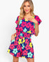 A woman modeling a short-sleeve romper with a colorful floral print on a solid white background.