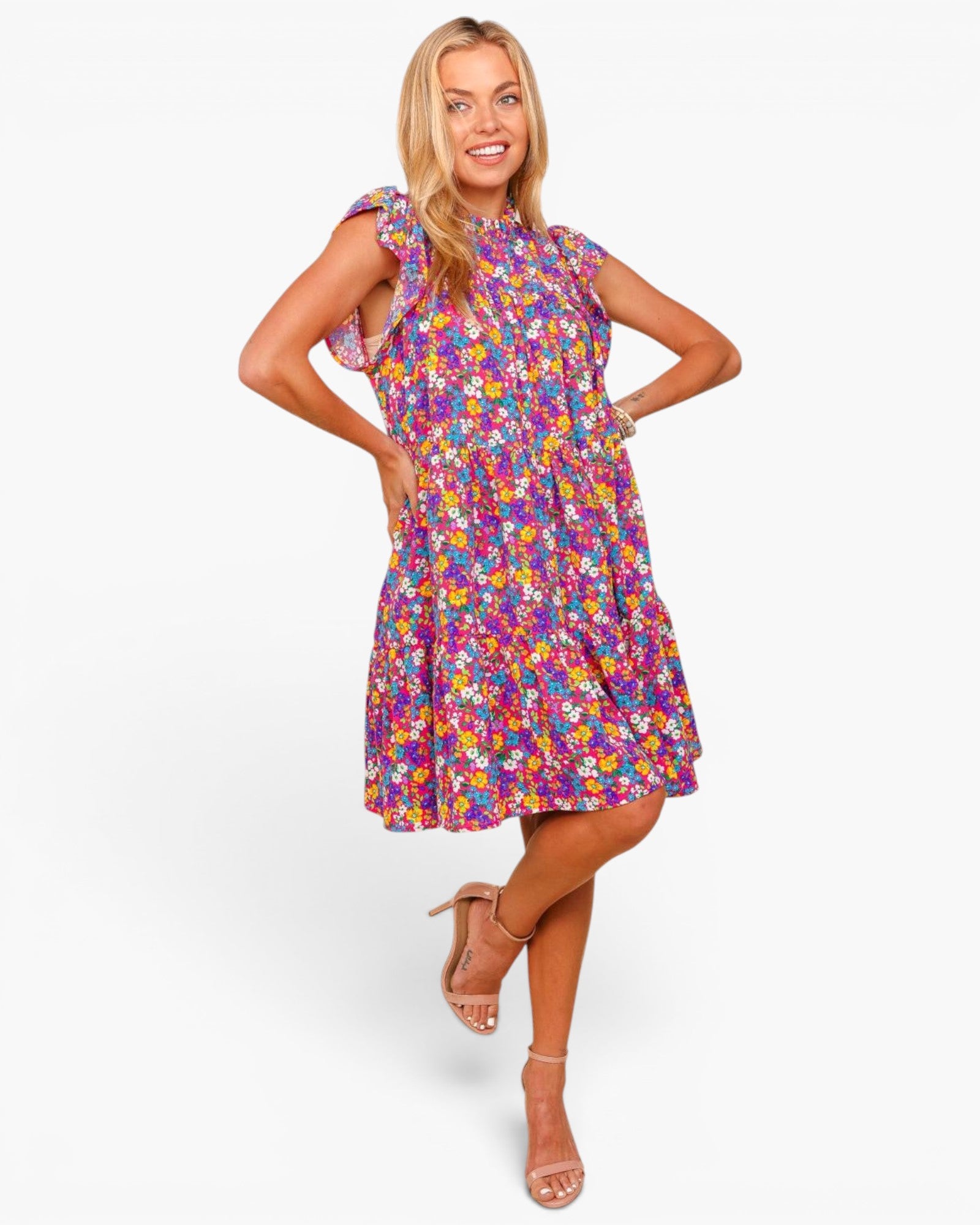 A woman modeling a sleeveless, knee-length dress with a colorful floral print on a light background, paired with beige strappy high-heeled sandals, against a plain white studio background.