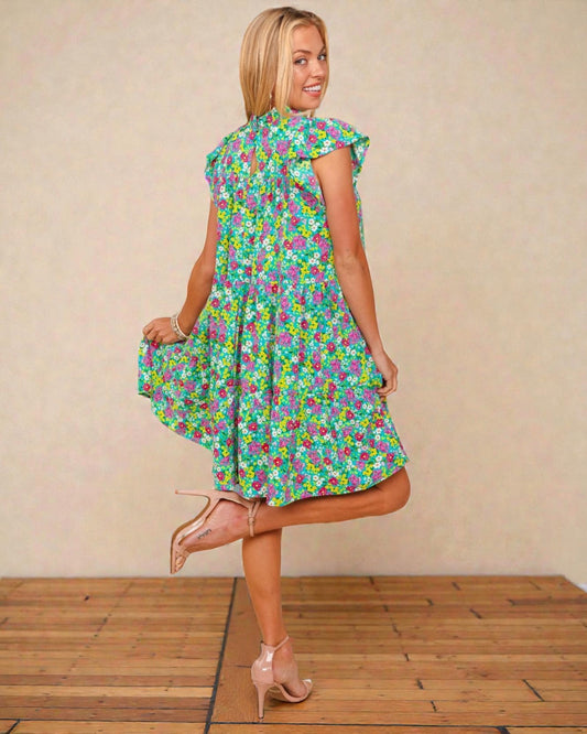 Woman wearing a colorful floral dress against a beige wall.