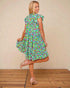 Woman wearing a colorful floral dress against a beige wall.
