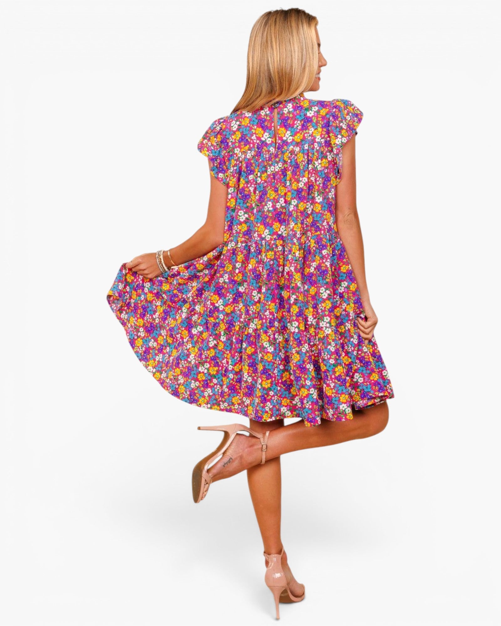 A woman modeling a short-sleeve, ruffled-skip dress with a vibrant multicolor floral print, shown from a back-three-quarter view against a plain white studio background.
