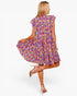 A woman modeling a short-sleeve, ruffled-skip dress with a vibrant multicolor floral print, shown from a back-three-quarter view against a plain white studio background.