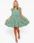 A woman modeling a short-sleeve, high-neck, flared mini dress with an all-over colorful floral print on a light green background, paired with beige strappy high-heeled sandals against a plain white studio background.