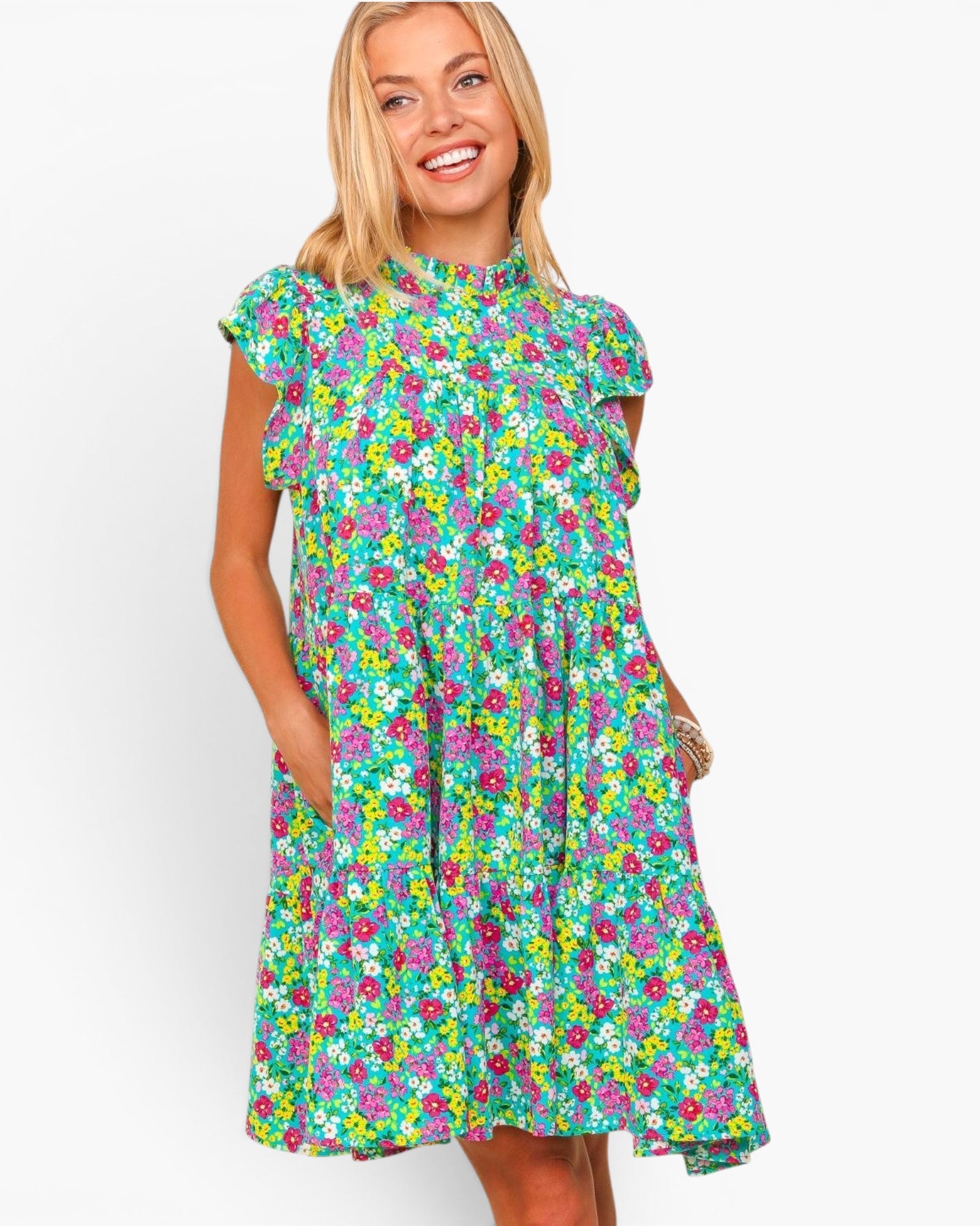 A woman wearing a short-sleeve, high-neck, knee-length dress with a colorful floral print on a green background, posed against a light gray studio background.