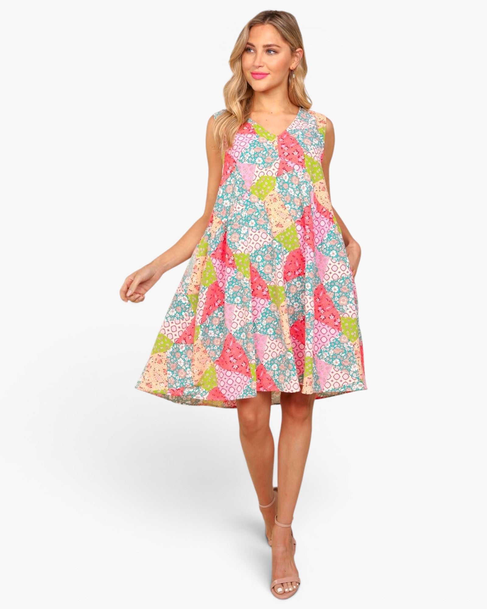 A woman modeling a sleeveless A-line dress with a colorful patchwork floral print, set against a plain light gray studio background.