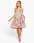 A woman modeling a sleeveless A-line dress with a colorful patchwork floral print, set against a plain light gray studio background.