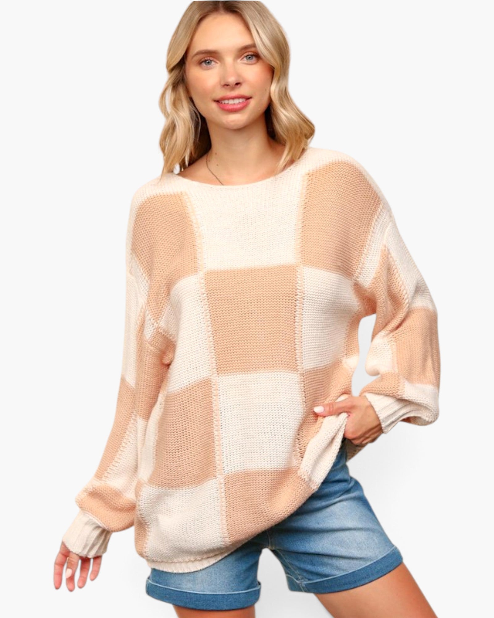 A woman wearing a chunky knit sweater with a large checkered pattern in beige and cream, paired with blue denim shorts, against a plain white background.