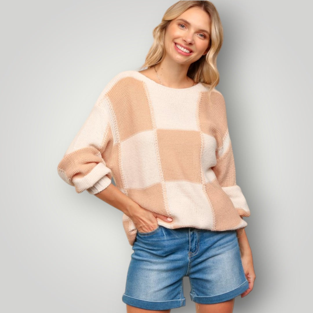 Woman wearing a patchwork sweater and denim shorts against a plain background