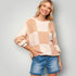 Woman wearing a patchwork sweater and denim shorts against a plain background