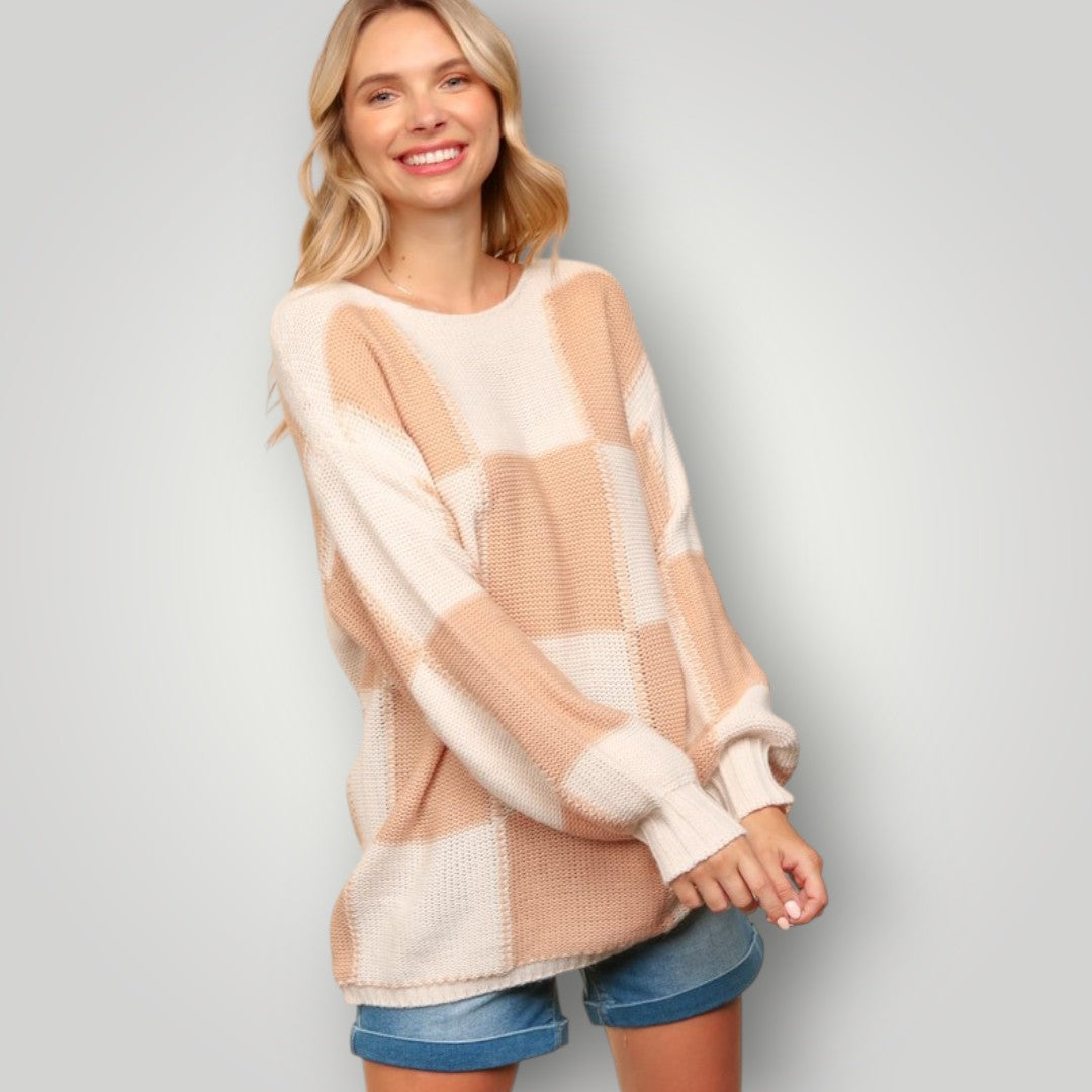 Woman wearing a beige and white checkered sweater with denim shorts on a plain background