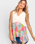 A woman modeling a sleeveless top with a solid cream upper section and a colorful patchwork floral hem in pink, green, and blue, paired with denim shorts against a light gray background.