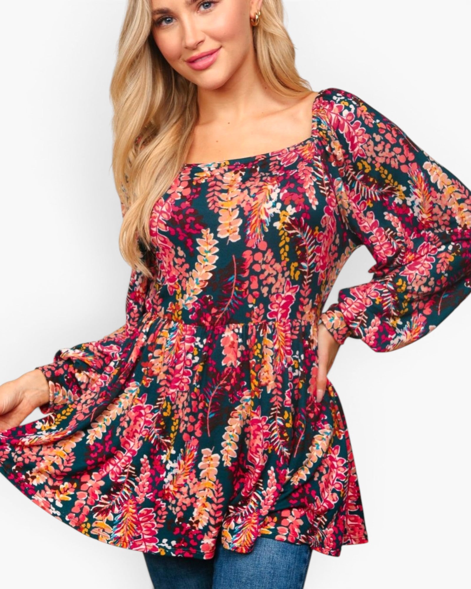 A woman wearing a long-sleeve peplum top with a vibrant multicolor floral and leaf print on a dark background, paired with blue jeans, against a plain white studio background.