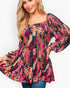 A woman wearing a long-sleeve peplum top with a vibrant multicolor floral and leaf print on a dark background, paired with blue jeans, against a plain white studio background.