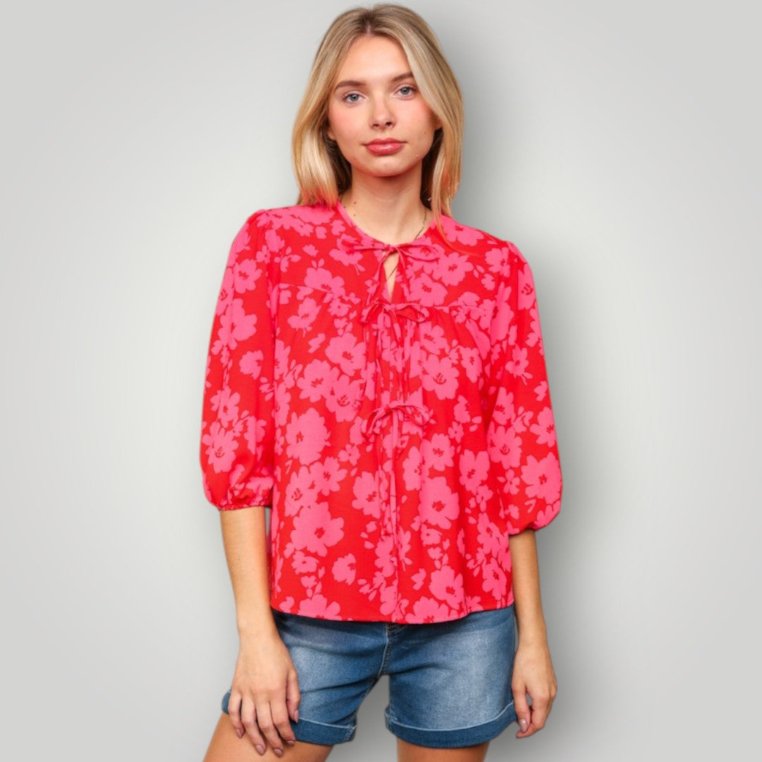 Woman wearing a red floral blouse and denim shorts on a gray background