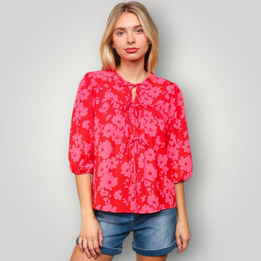 Woman wearing a red floral blouse and denim shorts on a gray background