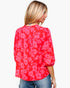 A woman shown from the back wearing a red and pink floral patterned blouse with three-quarter sleeves, paired with blue jeans, against a plain white background.