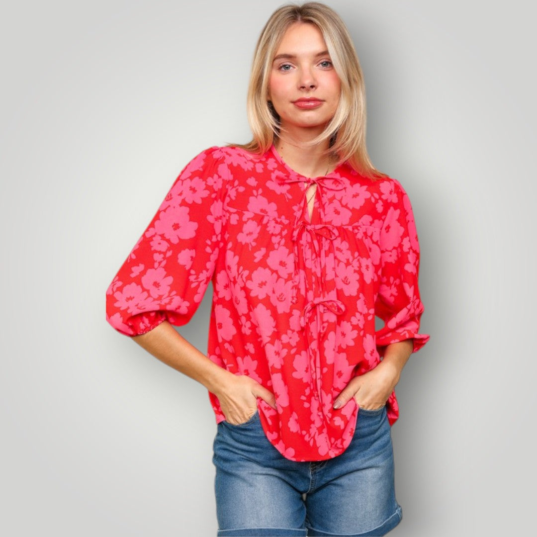 Woman wearing a red floral blouse and denim shorts against a plain background