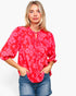 A woman wearing a red and pink floral print blouse with puff sleeves and a tie-neck detail, paired with blue denim shorts, against a plain white background.