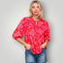 Woman wearing a red floral blouse and denim shorts against a plain background
