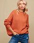 Woman wearing a rust-colored sweater and blue jeans against a beige background