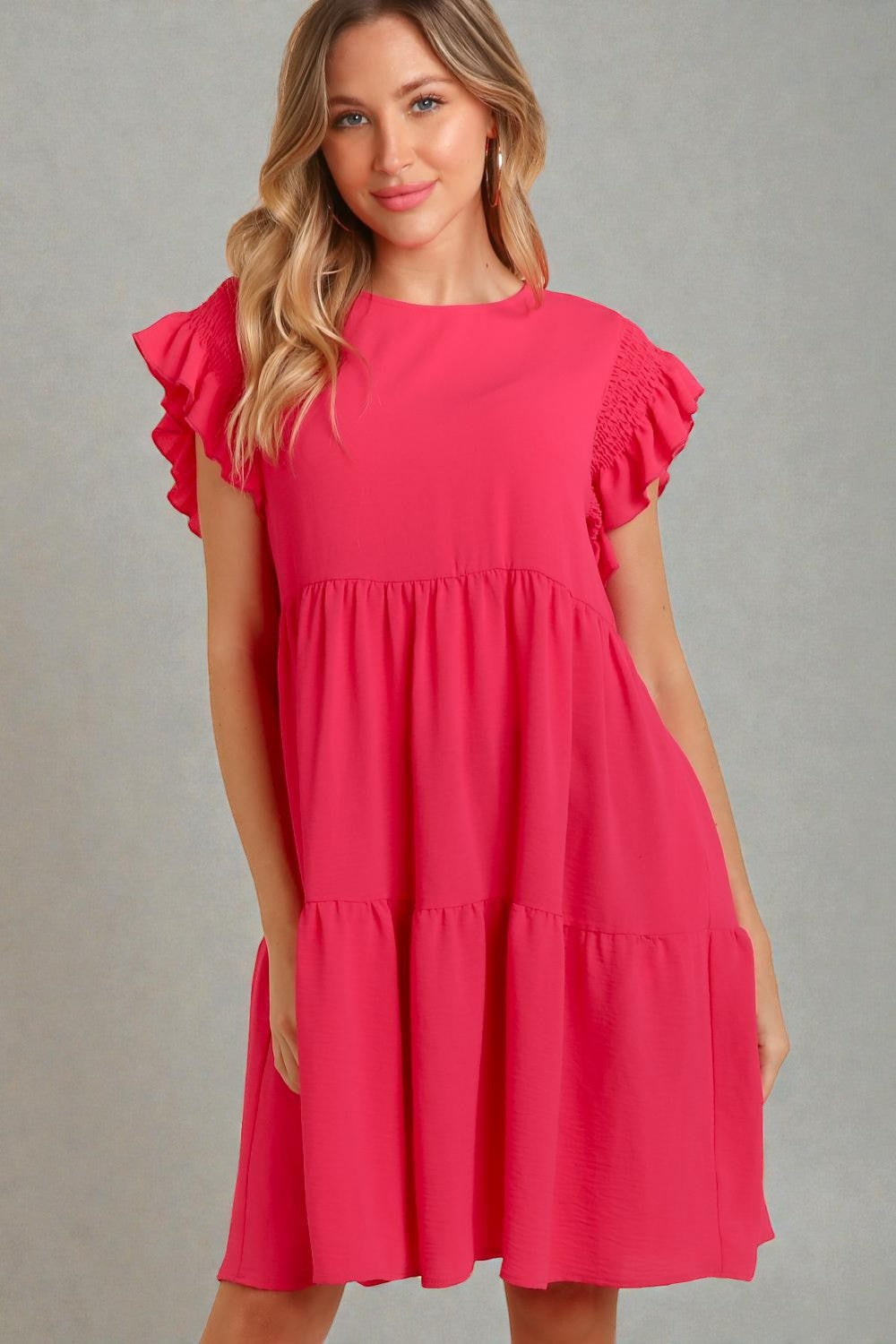 Woman wearing a pink dress with ruffled sleeves against a gray background