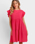 A woman wearing a bright pink tiered shift dress with ruffled cap sleeves and textured shoulder details, photographed against a light gray studio background.