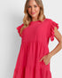 A woman wearing a bright pink tiered dress with ruffled short sleeves and side pockets, photographed against a light gray studio background.