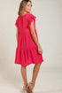 Woman wearing a pink dress with ruffled sleeves on a plain background