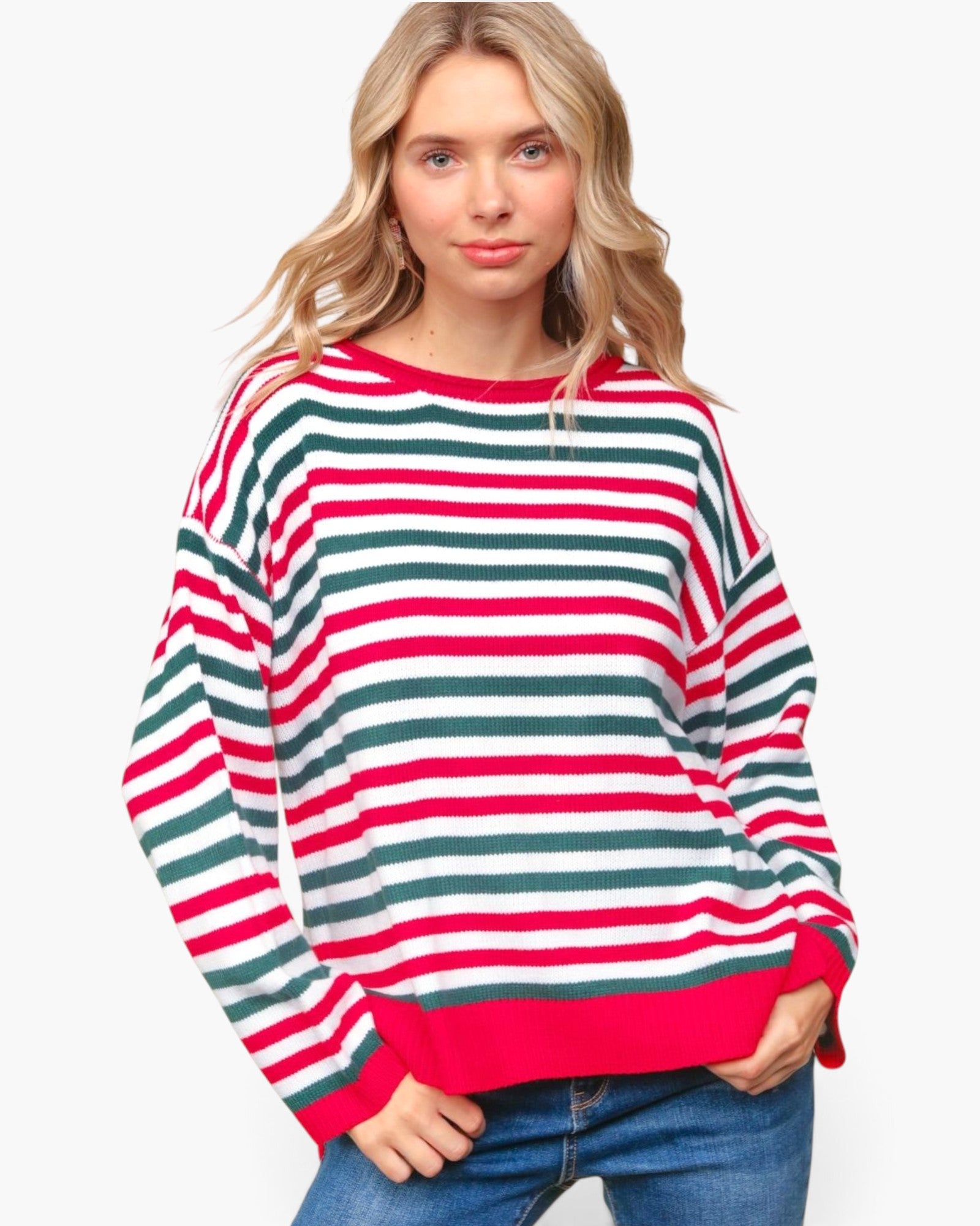 A woman wearing a long-sleeve knit sweater with horizontal red, green, and white stripes, paired with blue jeans, against a plain white background.