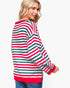 A woman wearing a long-sleeve knit sweater with horizontal red, green, and white stripes, shown from a three-quarter back view against a light gray studio background.
