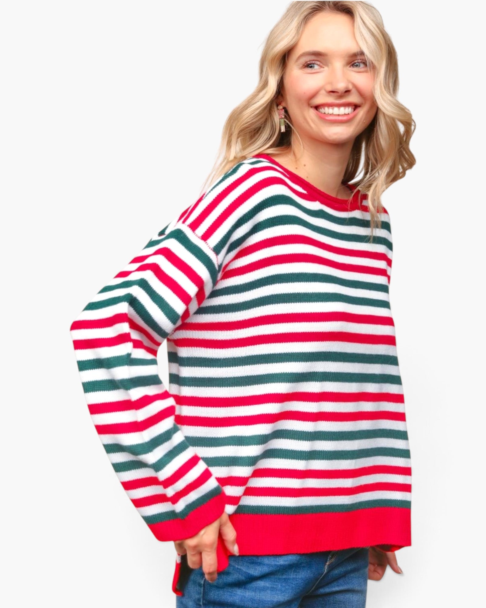 A woman wearing a long-sleeve knit sweater with horizontal red, green, and white stripes, paired with blue jeans, against a plain white background.