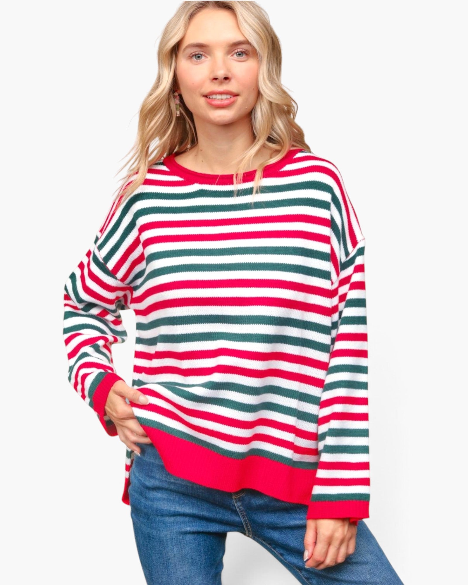 A woman wearing a long-sleeve knit sweater with horizontal red, green, and white stripes, paired with blue jeans, against a plain white background.