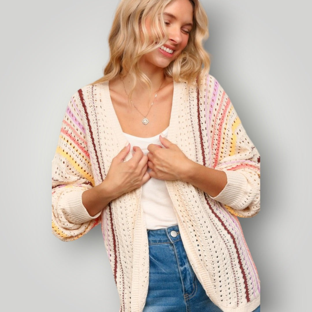 Woman wearing a colorful striped cardigan over a white shirt and blue jeans on a gray background