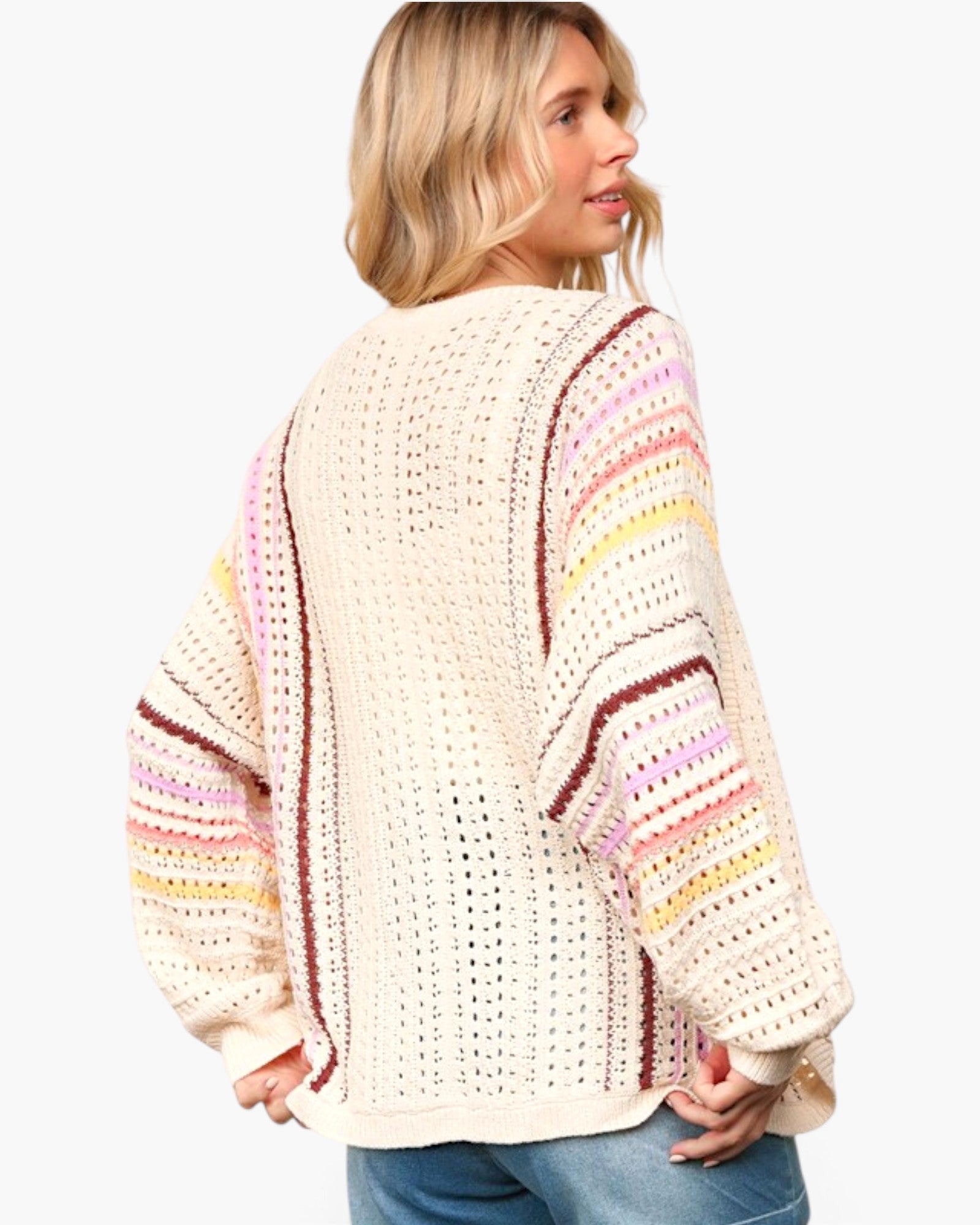 A woman wearing a cream-colored crochet knit sweater with pastel pink, yellow, and brown striped details on the sleeves, shown from a three-quarters back view against a light gray background.
