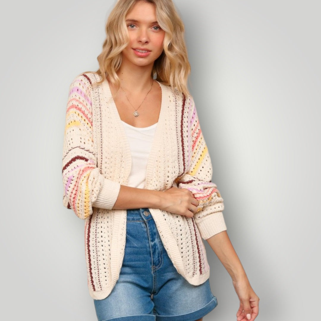 Woman wearing a colorful cardigan over a white top and blue shorts on a gray background