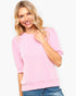 A smiling blonde woman wearing a light pink ribbed short-sleeve top and blue jeans, photographed against a clean white studio background.