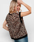 Woman wearing a leopard print top with black trim on a plain background