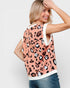 Woman wearing a pink leopard print top with a white trim on a plain background