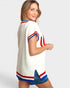 Woman wearing a white sweater with red and blue accents on a plain background