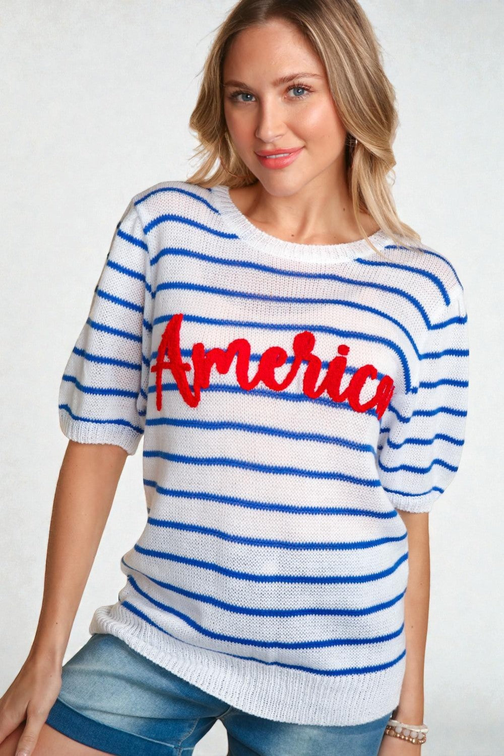 Woman wearing a white sweater with blue stripes and red text on a plain background